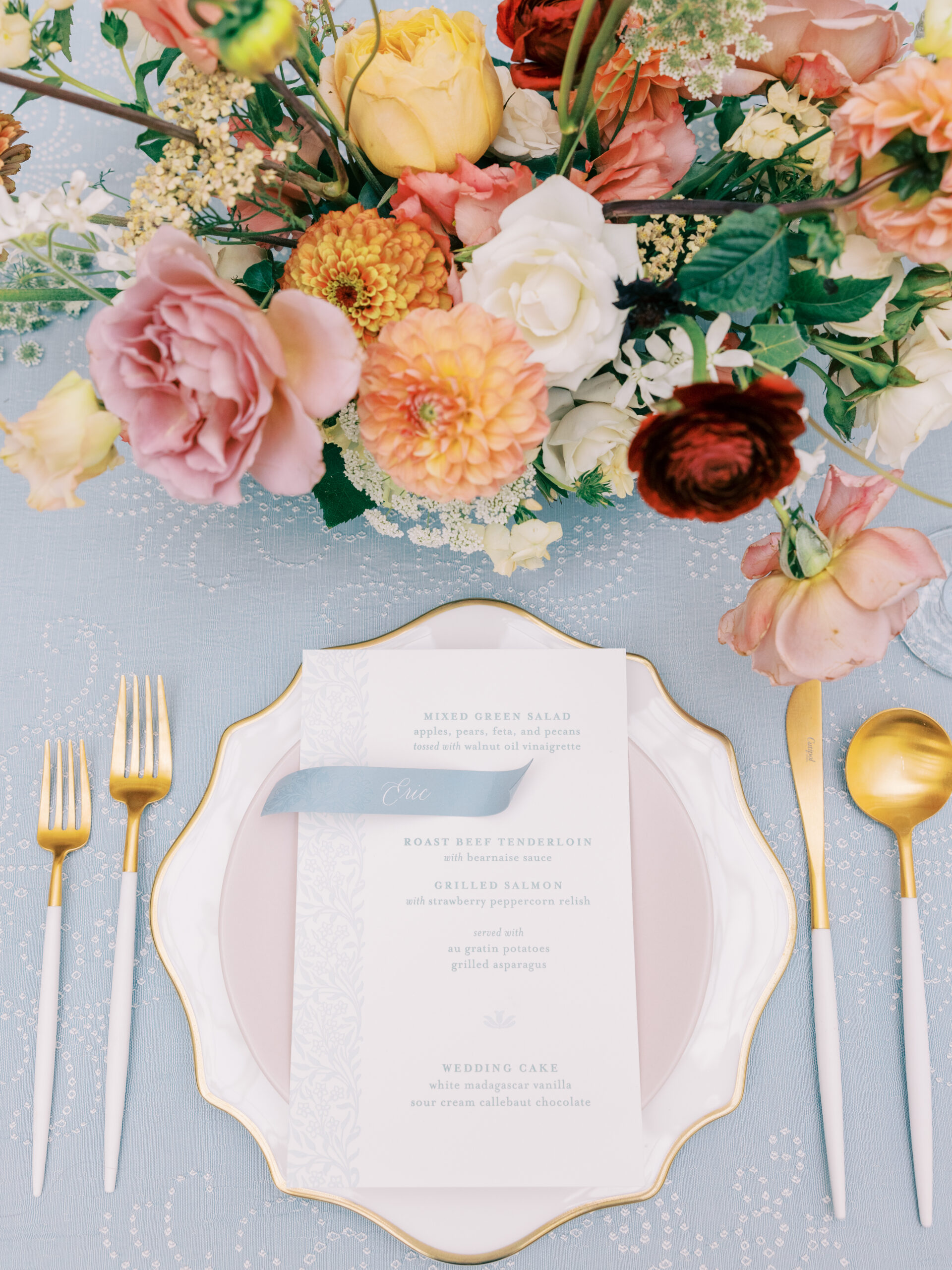 Detail photograph of wedding table setting with lush florals, gold ornate chargers and unique flatware